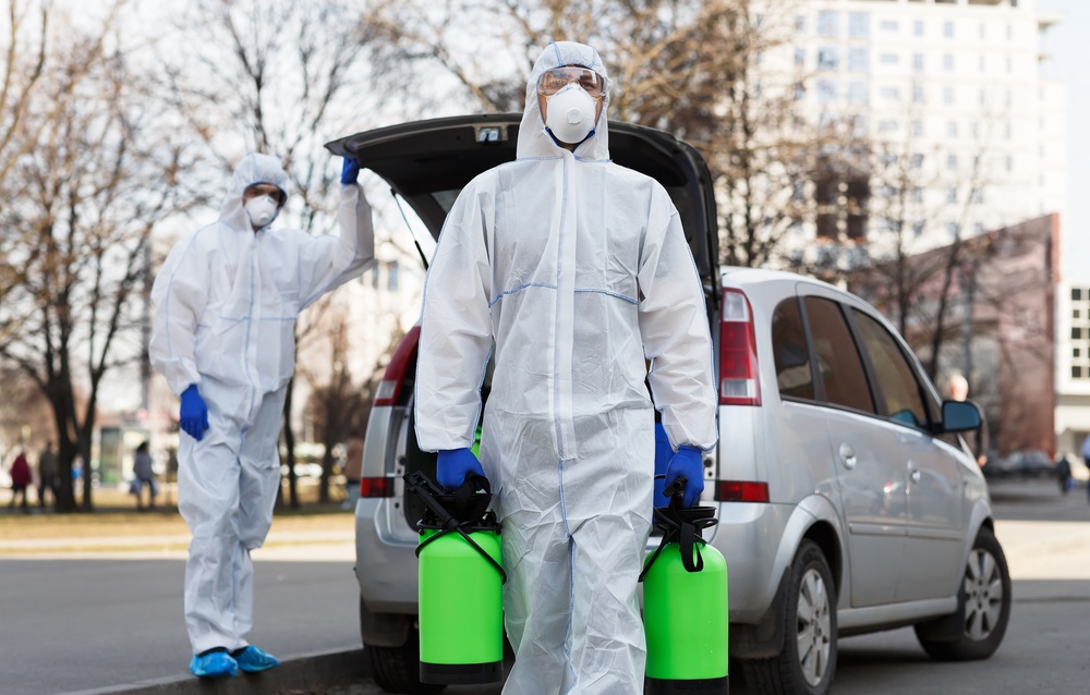 Two Adamant technicians in protective gear with sprayers beside the service vehicle