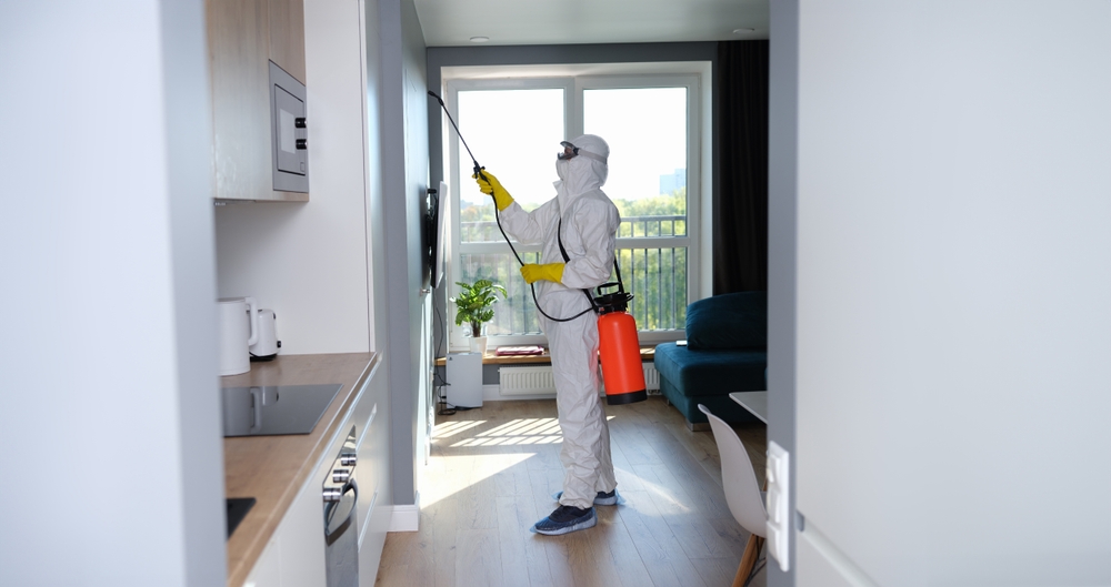 Technician in protective coveralls treating a window frame inside a home